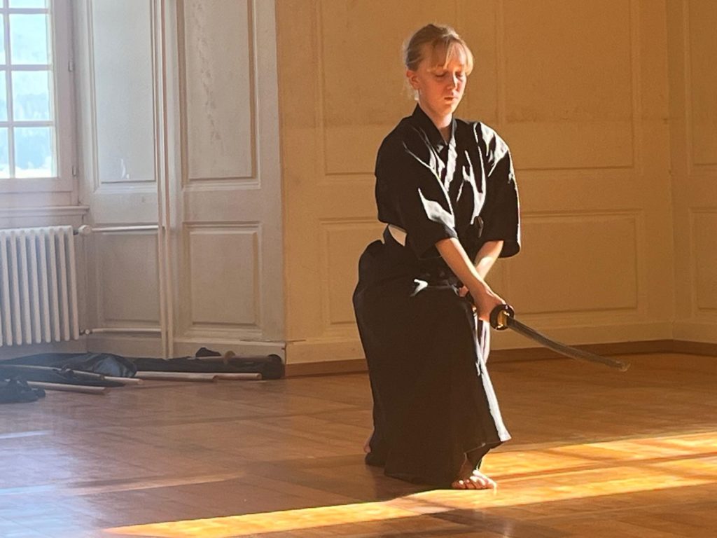 Laura, pratiquante de Muso Shinden Ryu, réalisant un kata de iaido au Dojo Tanren en Valais, démontrant la maîtrise du sabre et la concentration nécessaire dans cet art martial japonais ancestral.