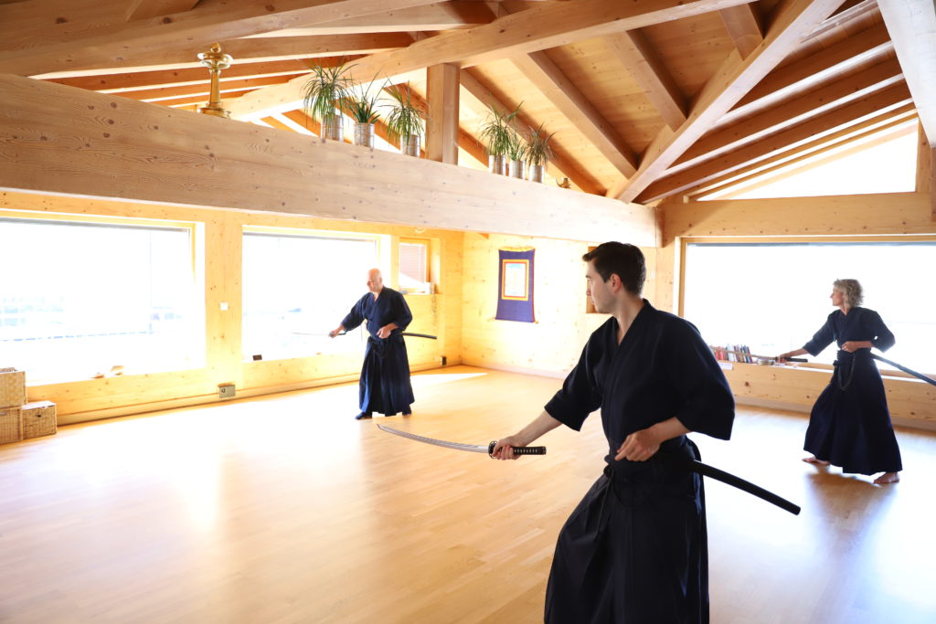 Trois pratiquants de Muso Shinden Ryu réalisant un kata de iaido dans le Dojo Tanren en Valais, illustrant la maîtrise du sabre et la discipline de cet art martial traditionnel.